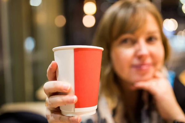 Lezzetli kahve içen bir kadın. Tatmin olmuş bir kadın gülümsüyor ve taze öğütülmüş bir fincan kahve içiyor. Kahve dükkânı konsepti. Kadınlar sabahları taze kahveyi sever. Bulanık filtre. Seçici odak. 
