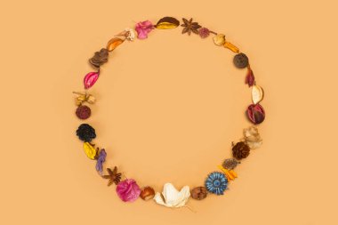 Kuru çiçeklerle yapılmış bir daire ve kahverengi bir arkaplanda üstten görünen yapraklar.