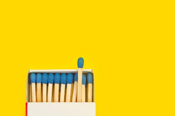 Wooden match stick with blue head in a match box on a yellow backgroud and copy space
