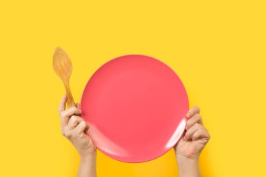 İki eli de sarı arka planda pembe bir tabak tutan kadın.