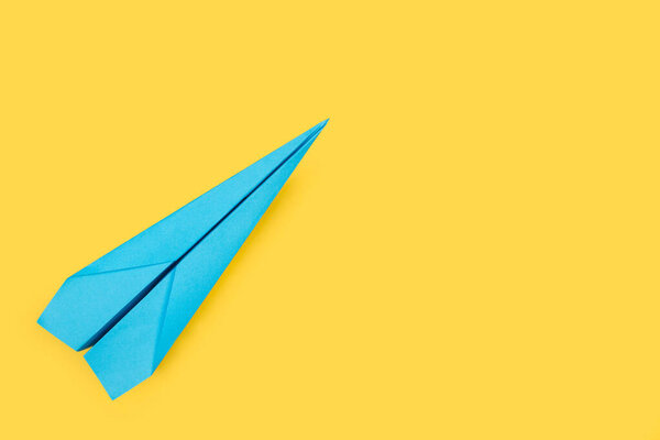 A blue paper plane on a yellow background with copy space