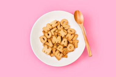 Alfabe harfleri beyaz bir tabakta pembe arka planda kurabiyeler. 