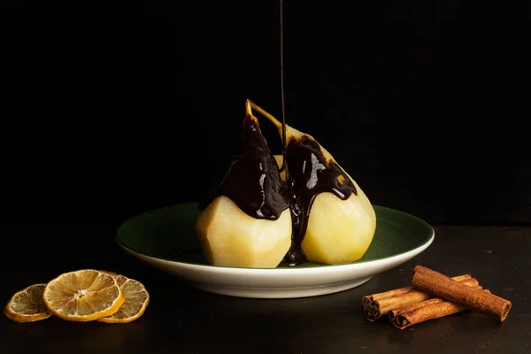 Dripping chocolate syrup on baked pears on a green plate in a dark background