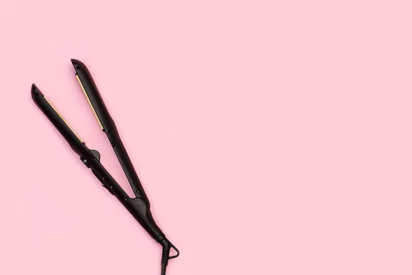 粉色背景上带有复制空间的黑发矫直机 — 图库照片