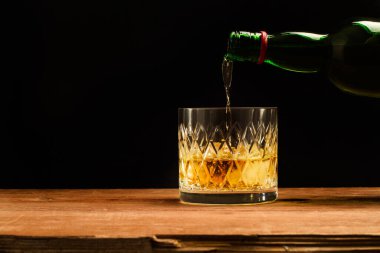 Bir bardak viskiyi ahşap bir masaya ve karanlık bir arka plana dökerek