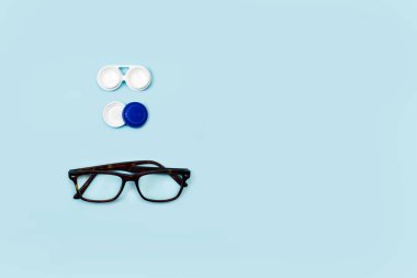 Üst görünümde mavi bir arkaplanda kontak lens kutusu ve gözlük