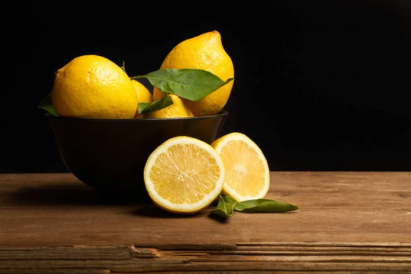 Lemons in a black bowl on a wooden table and on a black background