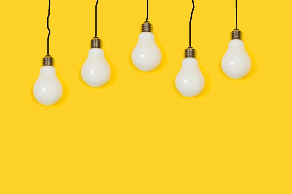 Lightbulbs hanging on a yellow background with copy space. Black lines like cables.