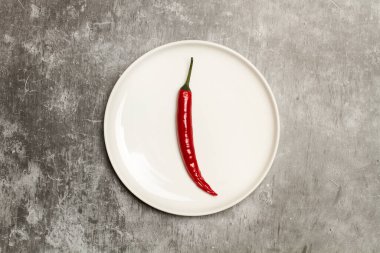 Kırmızı kırmızı kırmızı biber, beyaz tabakta taştan bir arka planda.