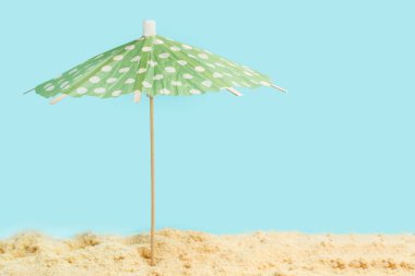 Kumun üzerinde beyaz noktalı yeşil bir şemsiye ve açık mavi bir arka plan.