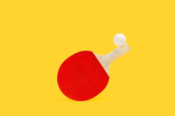黄色の背景に赤いピンポンパドルと白いボール — ストック写真