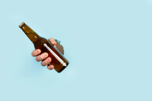 Homem Mão Segurando Uma Garrafa Cerveja Através Buraco Fundo Azul — Fotografia de Stock