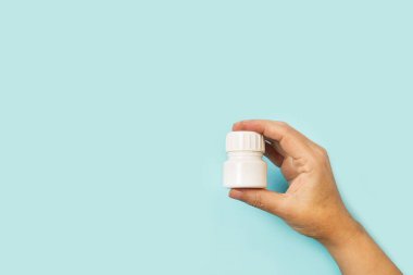 Açık mavi arka planda plastik bir tıbbi şişeyi tutan bir adam.