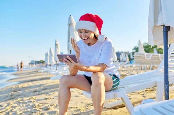 Nowy rok i święta Bożego Narodzenia, szczęśliwa kobieta w kapeluszu Świętego Mikołaja na plaży podejmowania rozmowy wideo — Zdjęcie stockowe