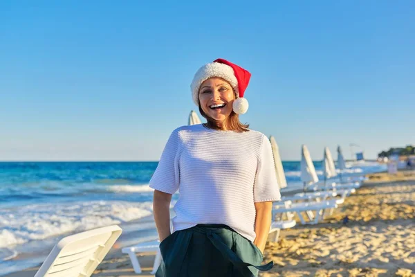 Πορτρέτο της ώριμης ευτυχισμένη γυναίκα στο καπέλο Σάντα στην παραλία θέρετρο — Φωτογραφία Αρχείου