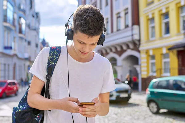 Подросток в наушниках с рюкзаком смотрит в экран смартфона — стоковое фото