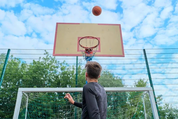 Adolescente chico saltar con pelota jugando baloncesto calle, vista trasera — Foto de Stock