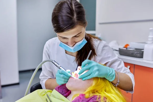 Dentista femenina tratando dientes a paciente, mujer joven en silla en clínica dental — Foto de Stock