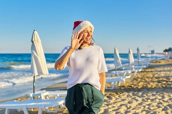 Πορτρέτο της ώριμης ευτυχισμένη γυναίκα στο καπέλο Σάντα στην παραλία θέρετρο — Φωτογραφία Αρχείου