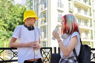 Neşeli konuşan öğrenciler şehirde şişeden yoğurt içiyorlar.