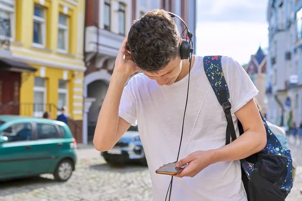 Подросток в наушниках с рюкзаком смотрит в экран смартфона — стоковое фото