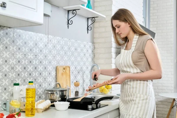 Молода красива жінка готує вдома на кухні, смажить яйця з сосисками — стокове фото