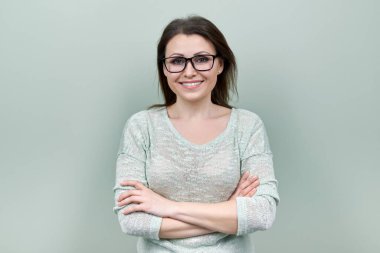 Orta yaşlı, gülümseyen, gözlüklü, yeşil arka planda çapraz kollu mutlu kadın.