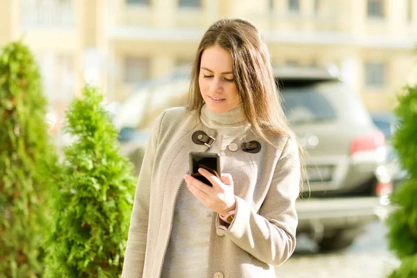 Красивая счастливая молодая женщина в пальто с телефоном на улице города — стоковое фото