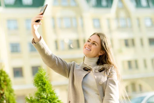 Piękna szczęśliwa młoda kobieta w płaszczu z telefonem na ulicy miasta — Zdjęcie stockowe