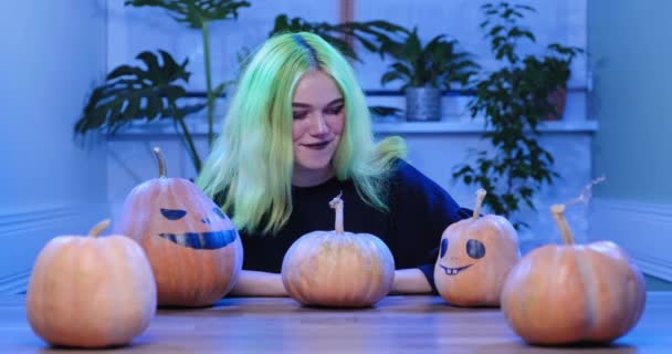 Хеллоуїн вечірка, дівчина-підліток з макіяжем, сидить за столом зі святковими декоративними гарбузами — стокове відео
