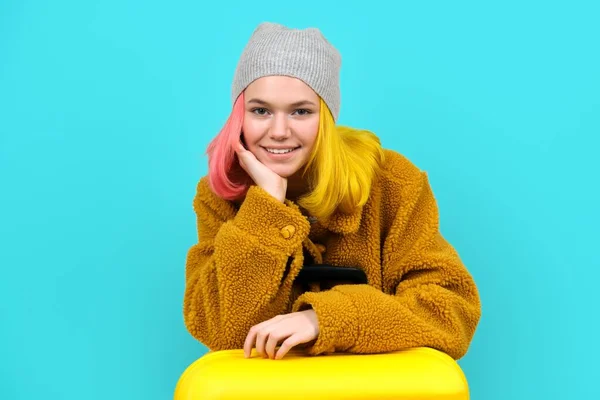 Teenager žena v klobouku kožich kabát s kufrem na modrém tyrkysovém pozadí — Stock fotografie