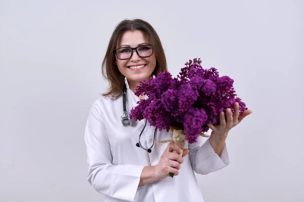 Bouquet of lilac flowers in the hands of female doctor with stethoscope