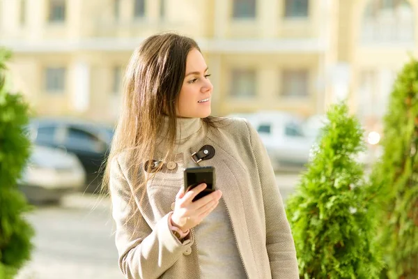 Молодая предпринимательница в осеннем городе в пальто со смартфоном на улице — стоковое фото