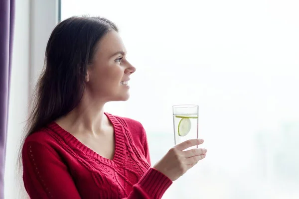 Молода усміхнена жінка зі склянкою води з лаймом — стокове фото