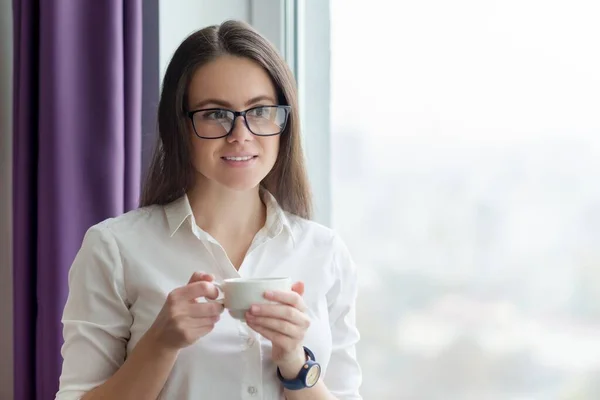 Jeune femme d'affaires avec tasse de café près de la fenêtre dans le bureau — Photo