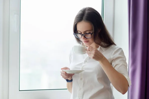 Jeune femme d'affaires avec tasse de café près de la fenêtre dans le bureau — Photo