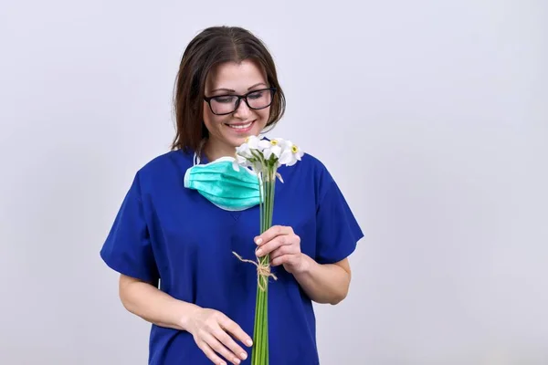 Portret van vrouwelijke arts verpleegkundige met verwijderde beschermende medische maskermet boeket bloemen — Stockfoto