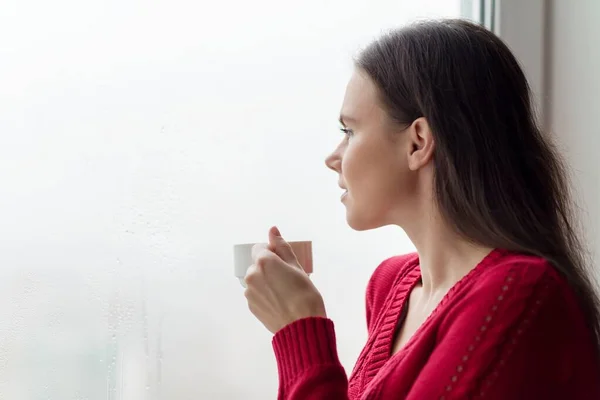 Joven mujer sonriente disfrutando del café, hembra en suéter de punto caliente cerca de la ventana — Foto de Stock