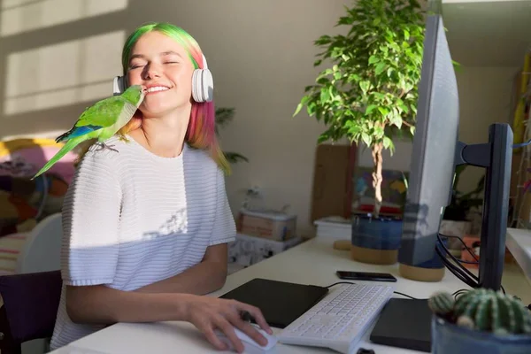 Studerande flicka i hörlurar studerar på dator med grafisk tablett, med papegoja — Stockfoto