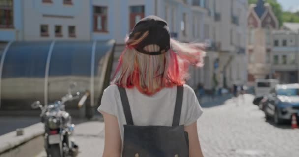 Fashionable beautiful teenager girl with trendy colorful hair walking along street of city, back view — Stock Video