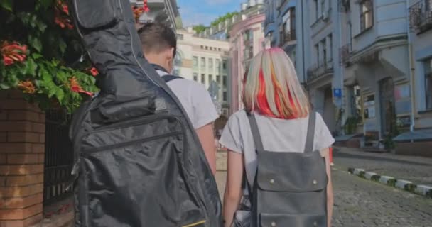 Trendy tienerhipsters jongen en meisje lopen praten op straat, jongen met gitaar in geval, achteraanzicht — Stockvideo