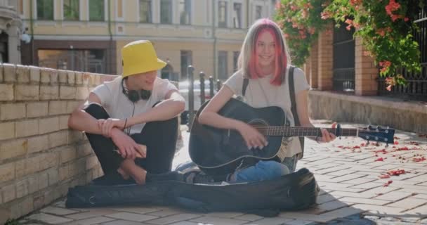 Niño y adolescente con una guitarra acústica en la calle de la ciudad, chica tocando la guitarra cantando con un amigo — Vídeos de Stock