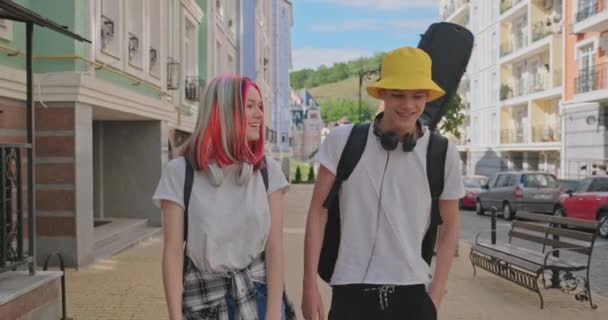 Trendy teenage hipsters boy and girl walking talking on city street, boy with guitar in case — Stock Video