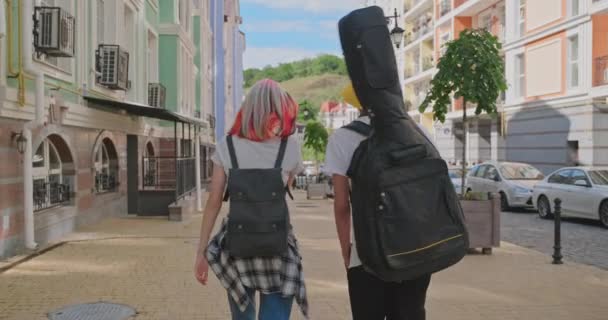 Trendig tonåring hipsters pojke och flicka promenader talar på stadens gata, pojke med gitarr i fall, baksida visa — Stockvideo