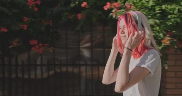 Szczęśliwa nastolatka hipster dziewczyna spaceruje na zewnątrz w słuchawkach słuchając audio, korzystając z muzyki — Wideo stockowe