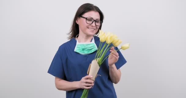 하얀 배경에 꽃다발을 댄 보호 의료용 마스크를 쓰고 간호사로 일하는 여의사. — 비디오