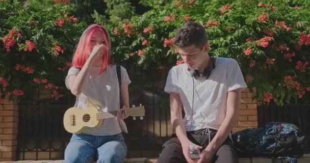 Pár teenagerských hipsterů venku, dívka hraje ukulele, kreativní trendy mládeže, hudba, koníčky a volný čas, městský teen životní styl — Stock video