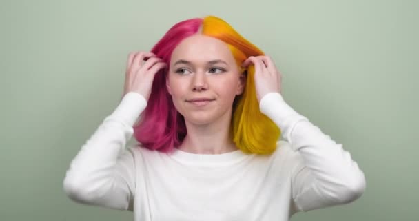 Menina adolescente sorridente bonita com penteado colorido na moda mostrando cabelo tingido e olhando para a câmera — Vídeo de Stock