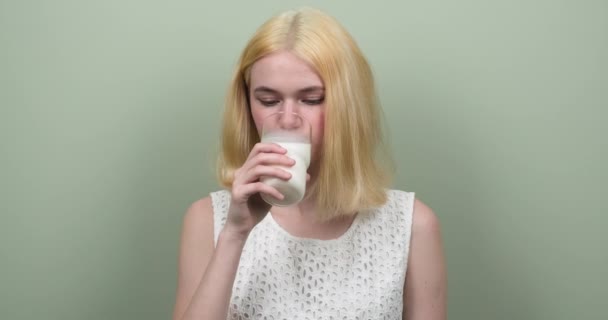 Flicka blond tonåring dricka mjölk från glas på ljusgrön bakgrund. Hälsosam mat, kost, ungdom, människor koncept — Stockvideo