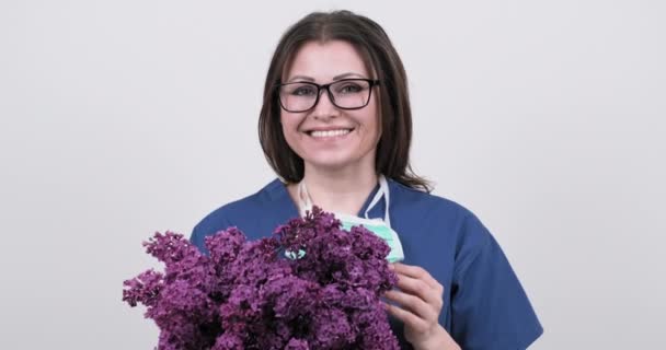 Portret dojrzałej uśmiechniętej lekarki w okularach z ochronną maską medyczną trzymającej bukiet kwiatów — Wideo stockowe